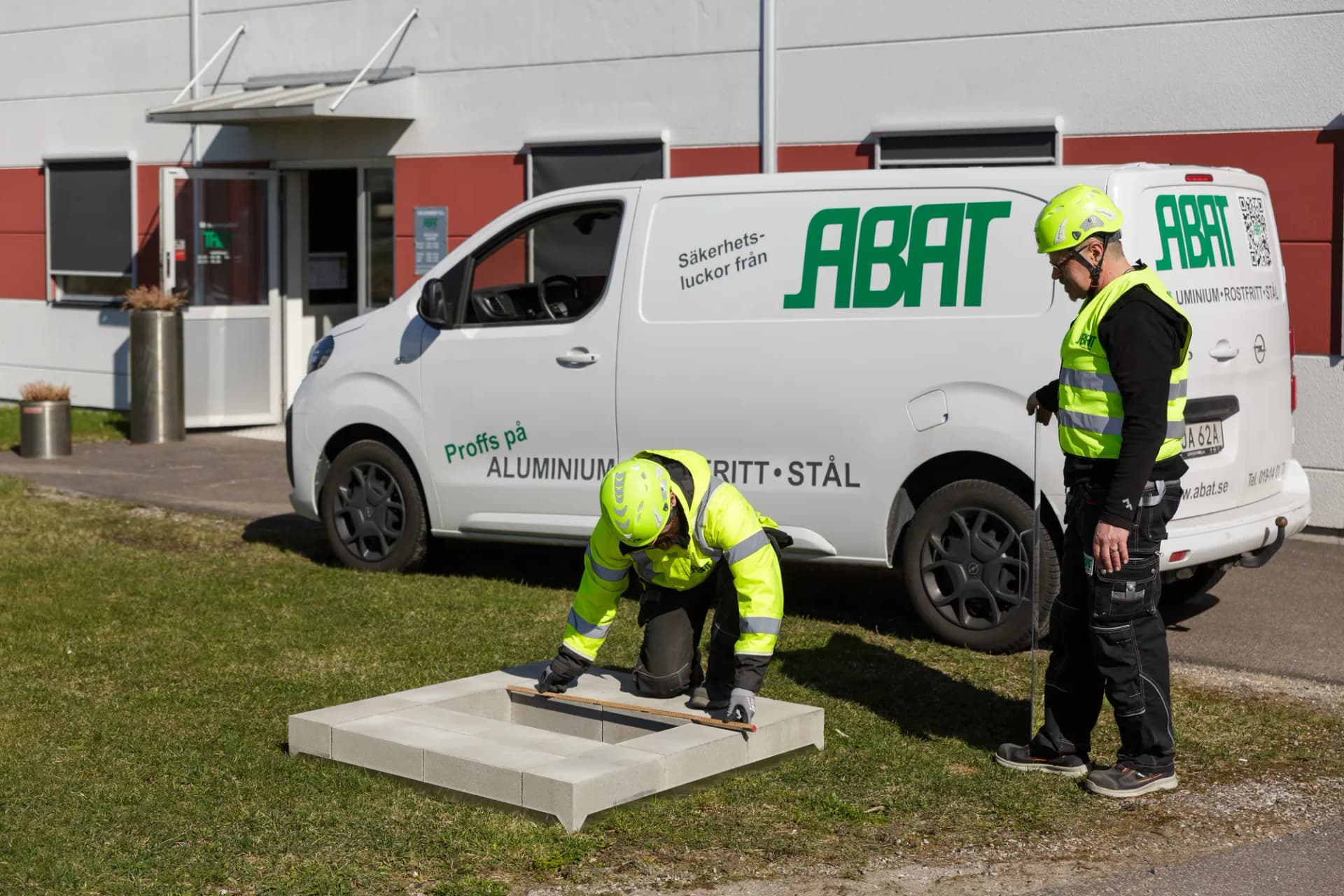 Två montörer från ABAT mäter in en luckram i marken framför servicebilen