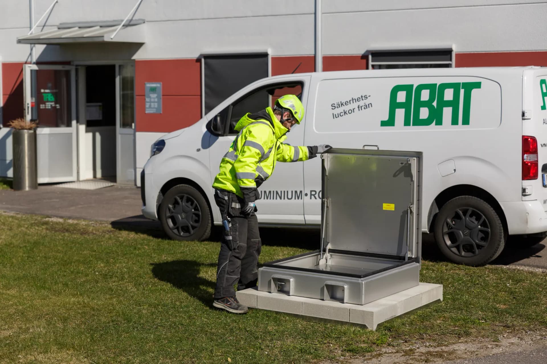 Montör vid en öppen rostfri säkerhetslucka framför ABAT:s servicebil